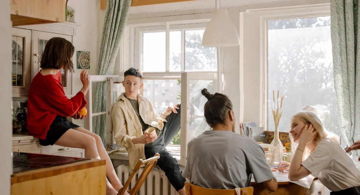 Group of young friends relaxing and chatting in a sunlit kitchen space.