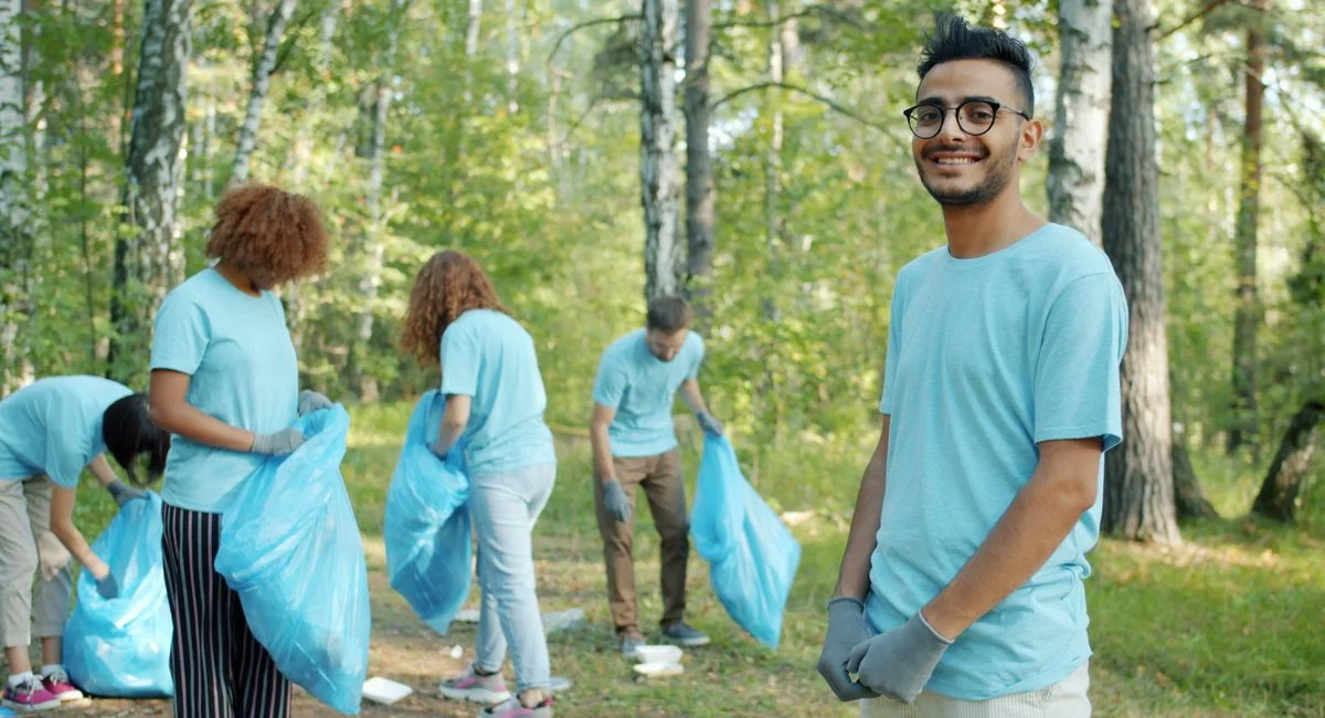 Diverse group of young volunteers cleaning up litter in a forest area on a sunny day.
