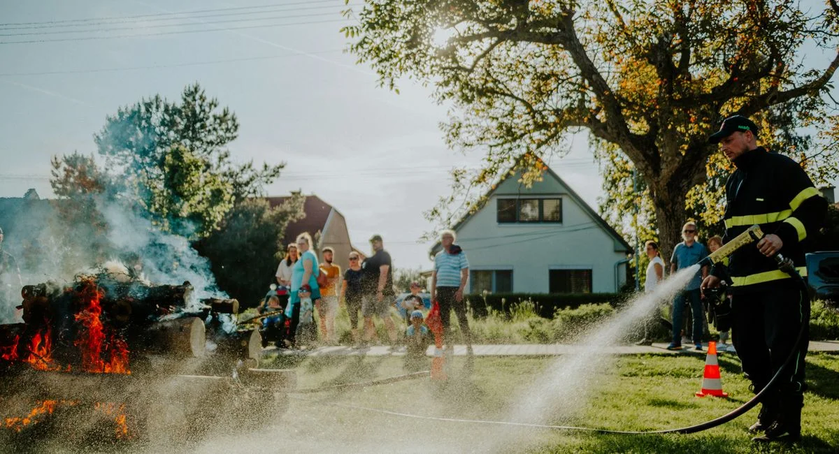 A firefighter extinguishes a controlled fire as a crowd watches during a demonstration on a sunny day.