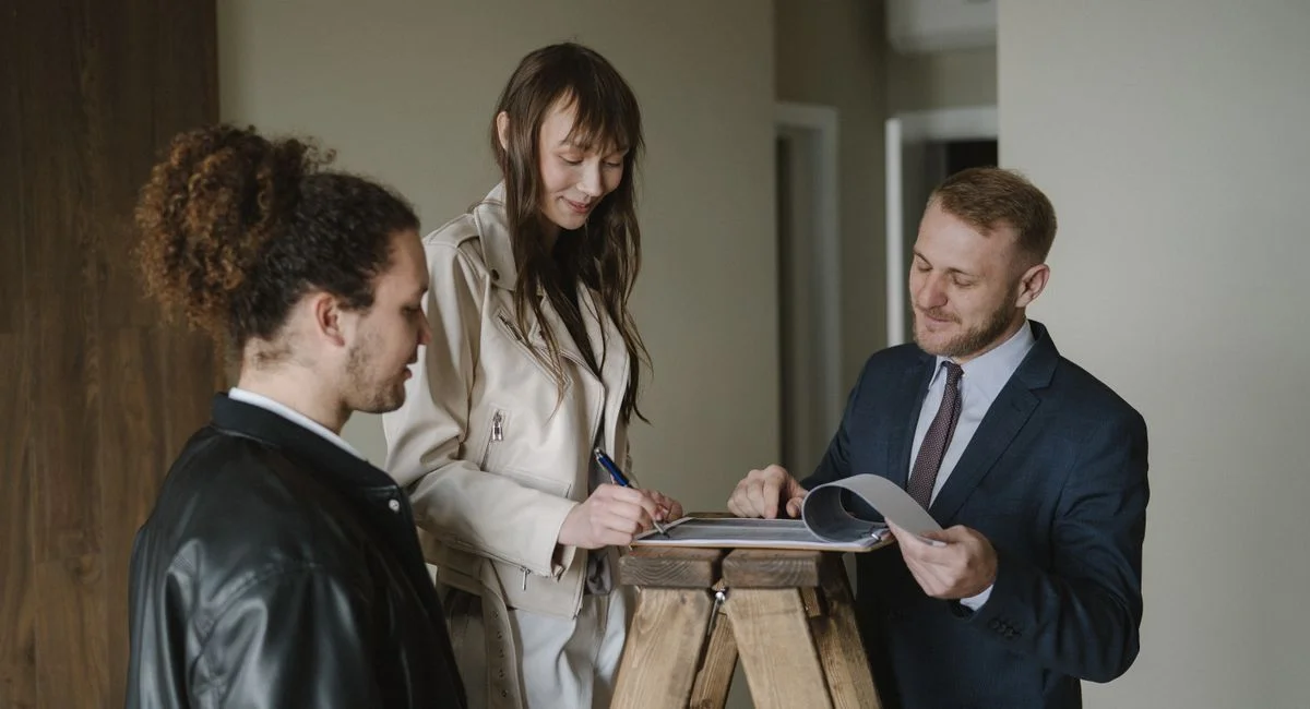 A couple signing real estate documents with a realtor inside a new apartment.