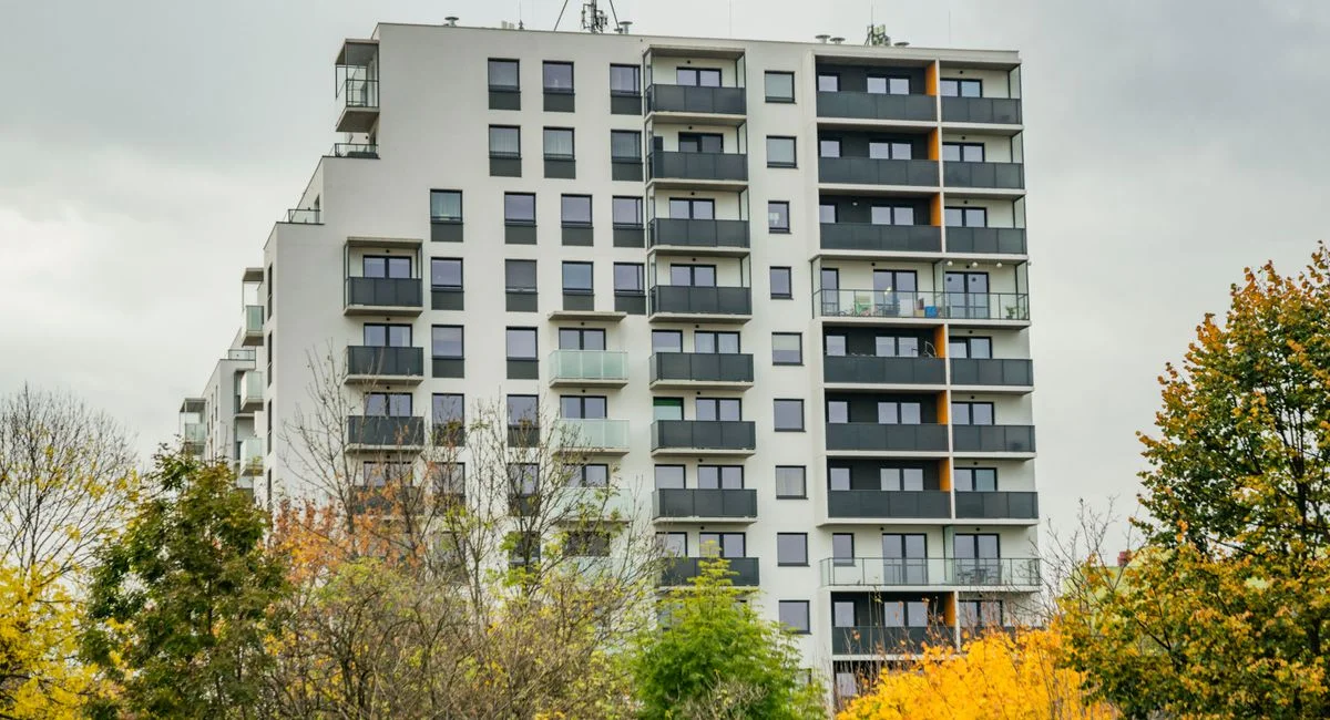High-rise apartment building surrounded by colorful autumn trees under cloudy skies.