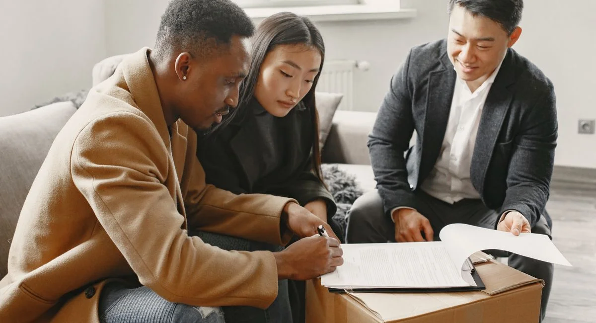 A multiracial couple signing home documents with a realtor indoors.