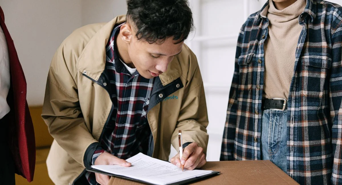 Young adults signing documents on moving day, finalizing new home purchase.