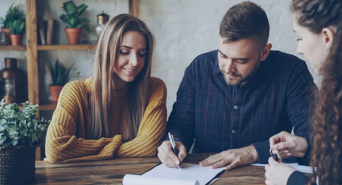 Three adults in a casual office setting reviewing and signing documents.