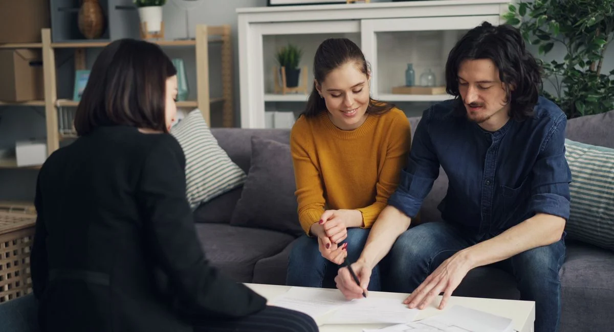 Three young adults working together at a home setting, signing documents.
