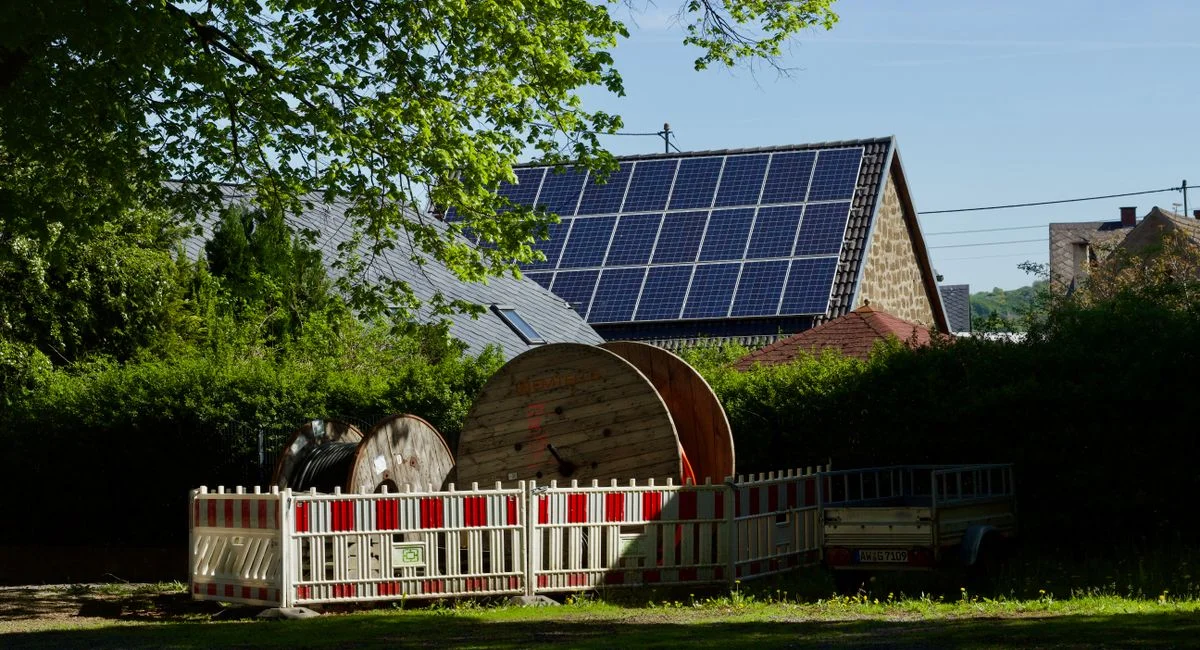 Barn with solar panels and cable reels in rustic countryside setting.