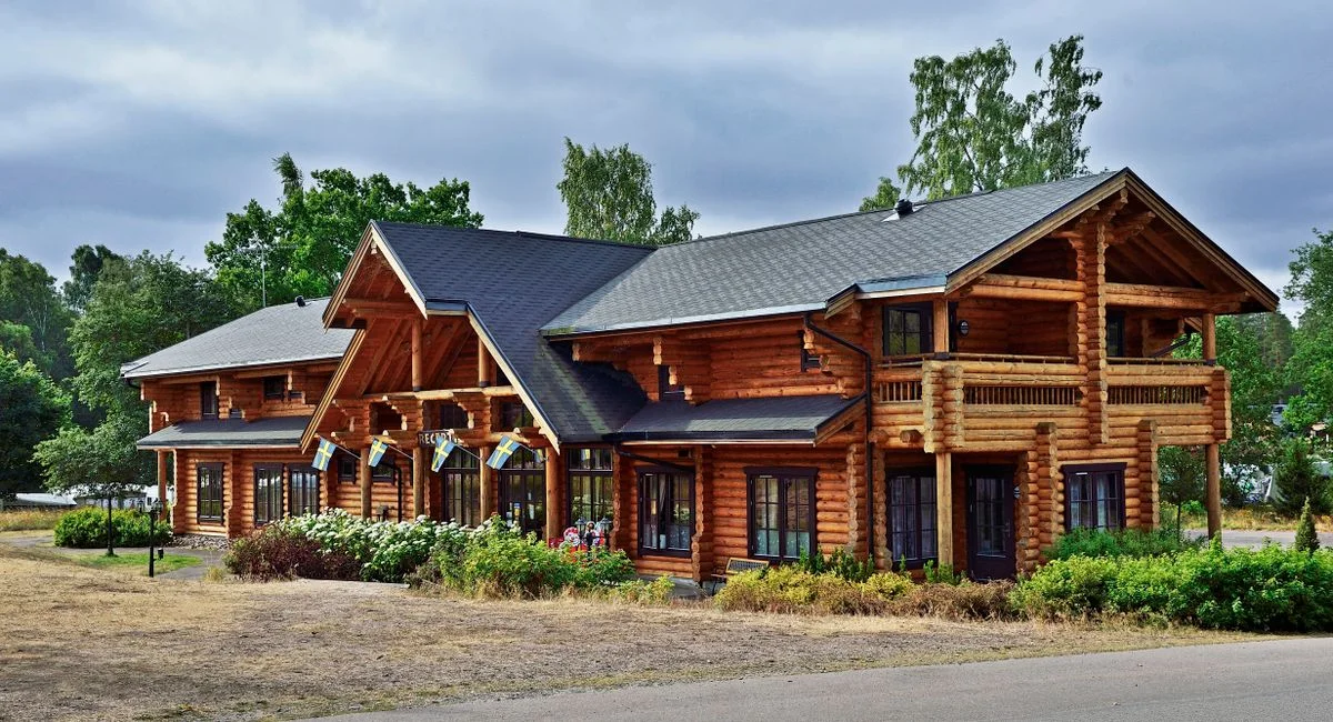 Traditional Scandinavian log cabin surrounded by lush greenery under a cloudy summer sky.