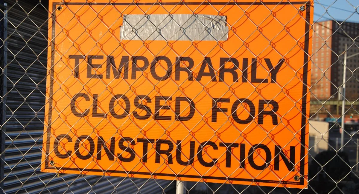 Orange sign behind fence reading 'Temporarily Closed for Construction' at site.