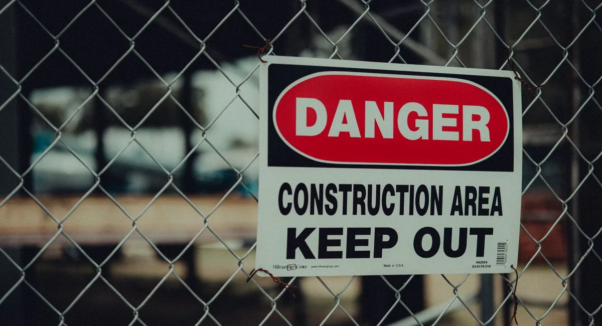 Close-up of a warning sign on a chain link fence at a construction site indicating danger.
