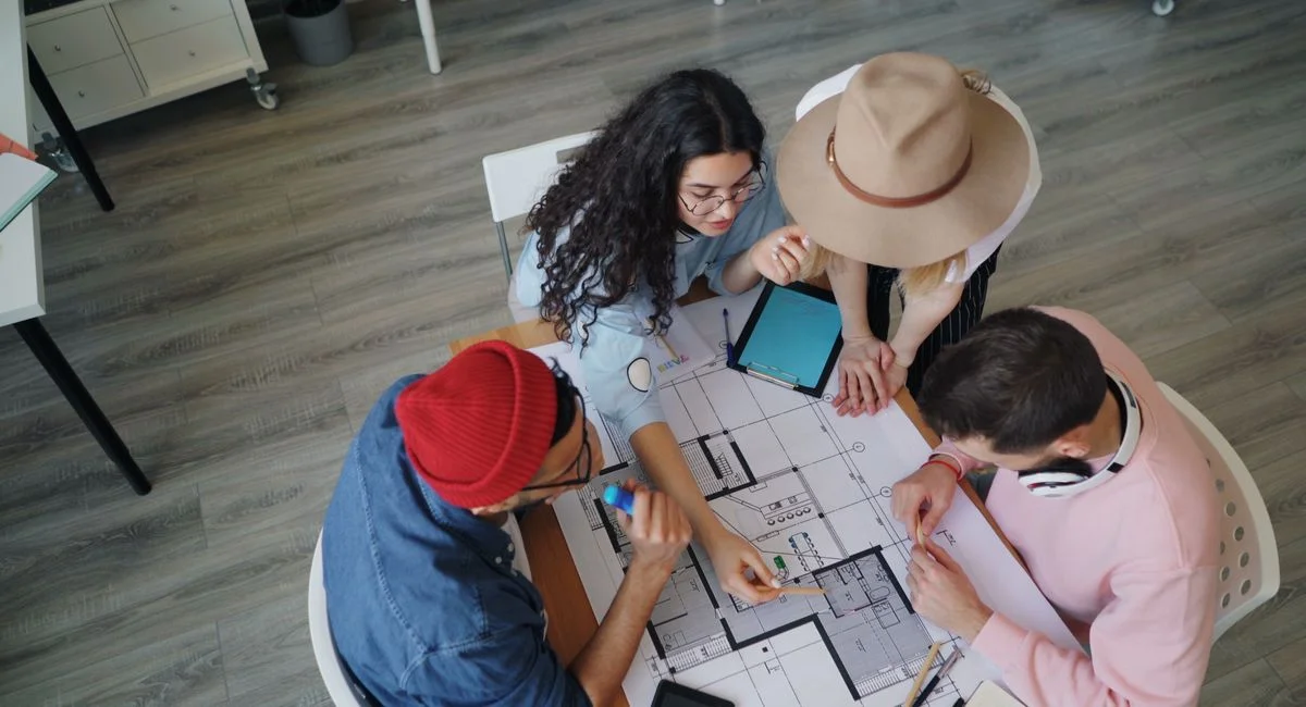 Four people collaborating over architectural blueprints in a modern office setting.
