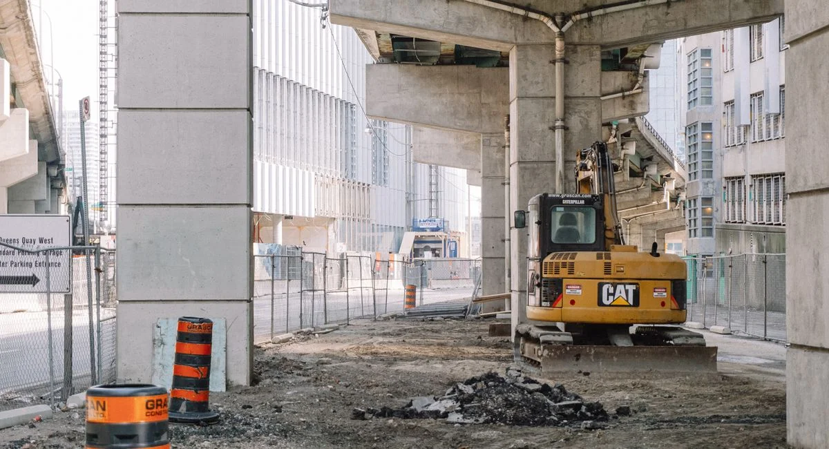 Site of roadway under concrete bridge construction with heavy equipment on dirty ground