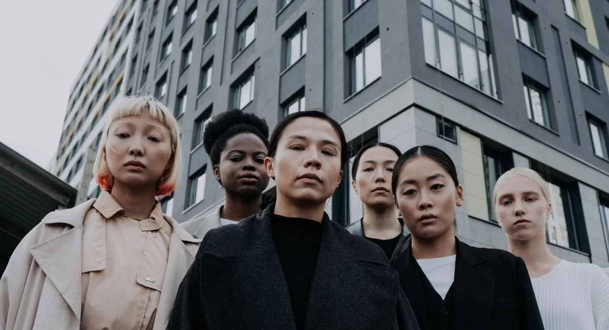 Strong and diverse group of women stand confidently in front of a modern apartment building.