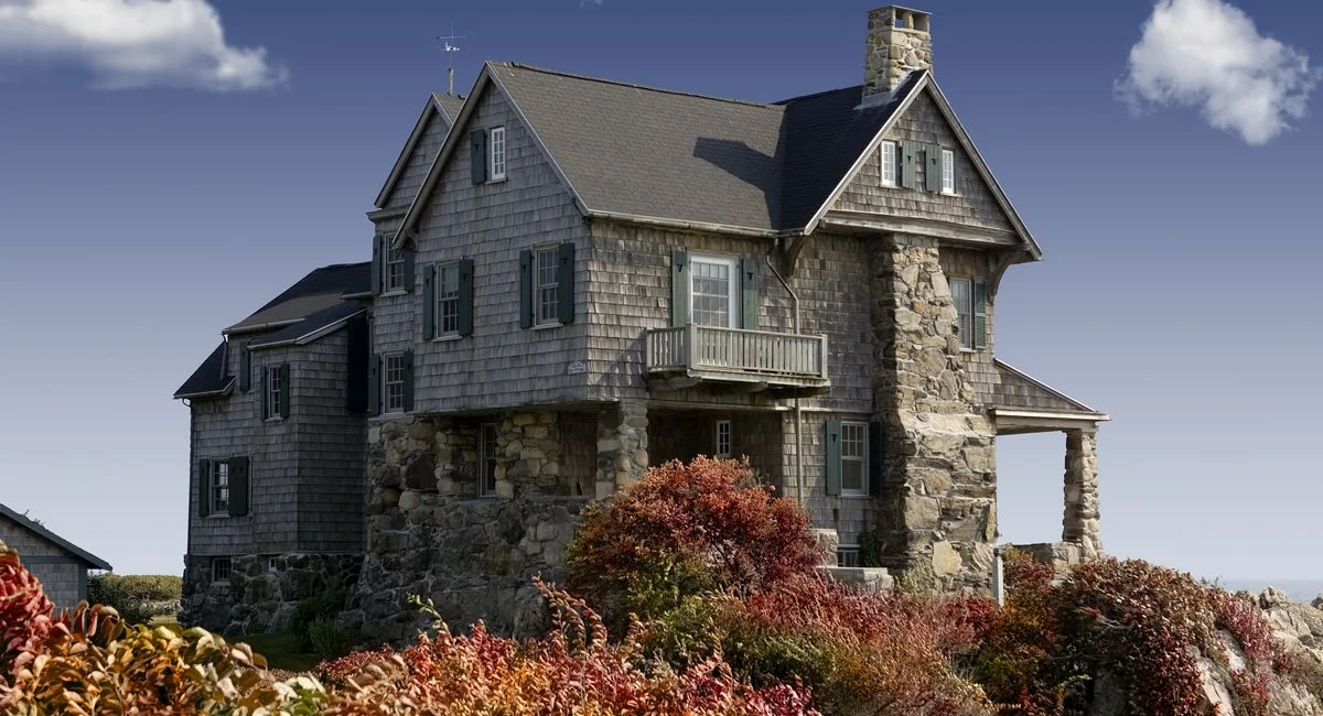 Charming old stone house surrounded by vibrant autumn foliage and clear blue sky.
