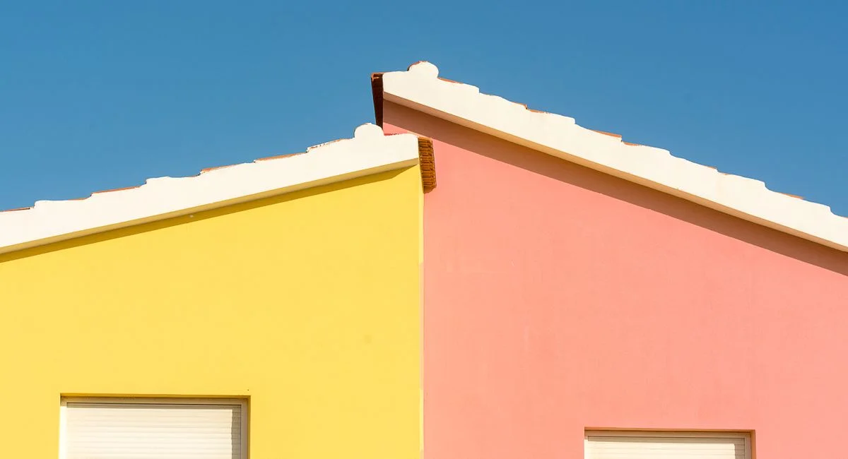 Close-up of vibrant yellow and pink house facades under a clear blue sky.