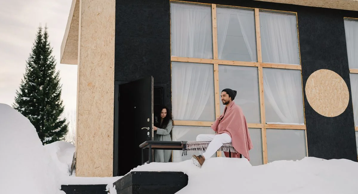 Contemporary house in a snowy setting with two people enjoying a winter day.