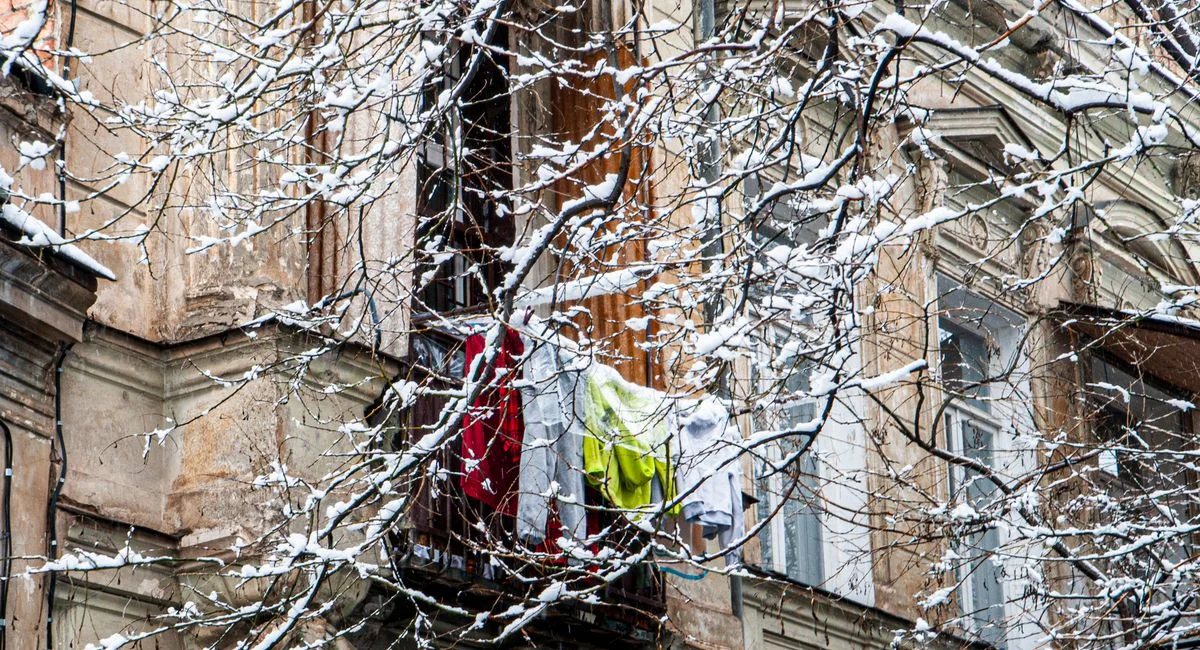 A historic Tbilisi balcony with clothes drying contrasts against a snowy urban backdrop.