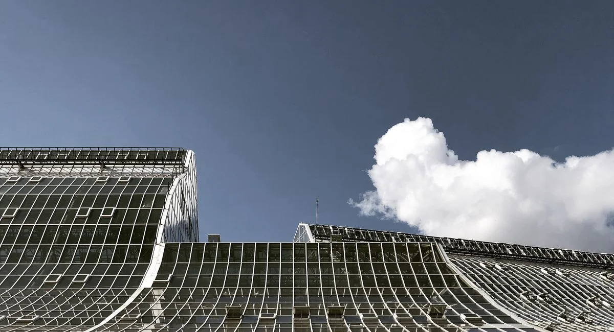 Curved glass architectural structure under a bright blue sky with white clouds in Moscow, Russia.