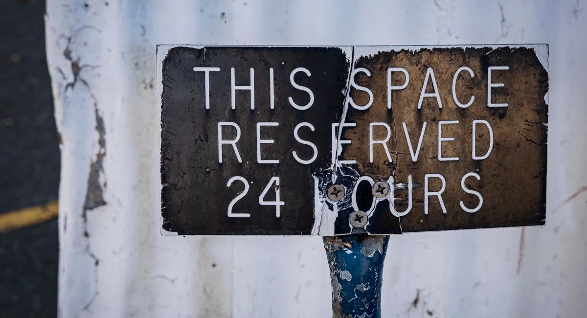 Rusted close-up of a weathered 'Reserved 24 Hours' parking sign in urban setting.