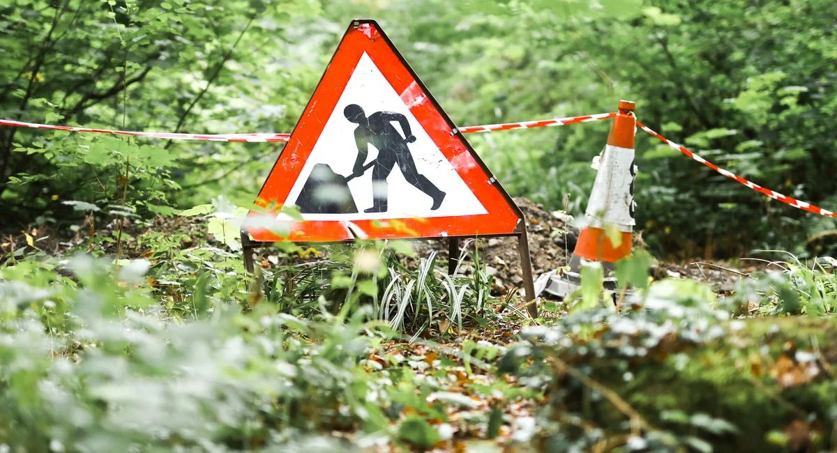 A road work sign in a forest setting in Ironbridge, UK, indicating an ongoing construction project amidst lush surroundings.