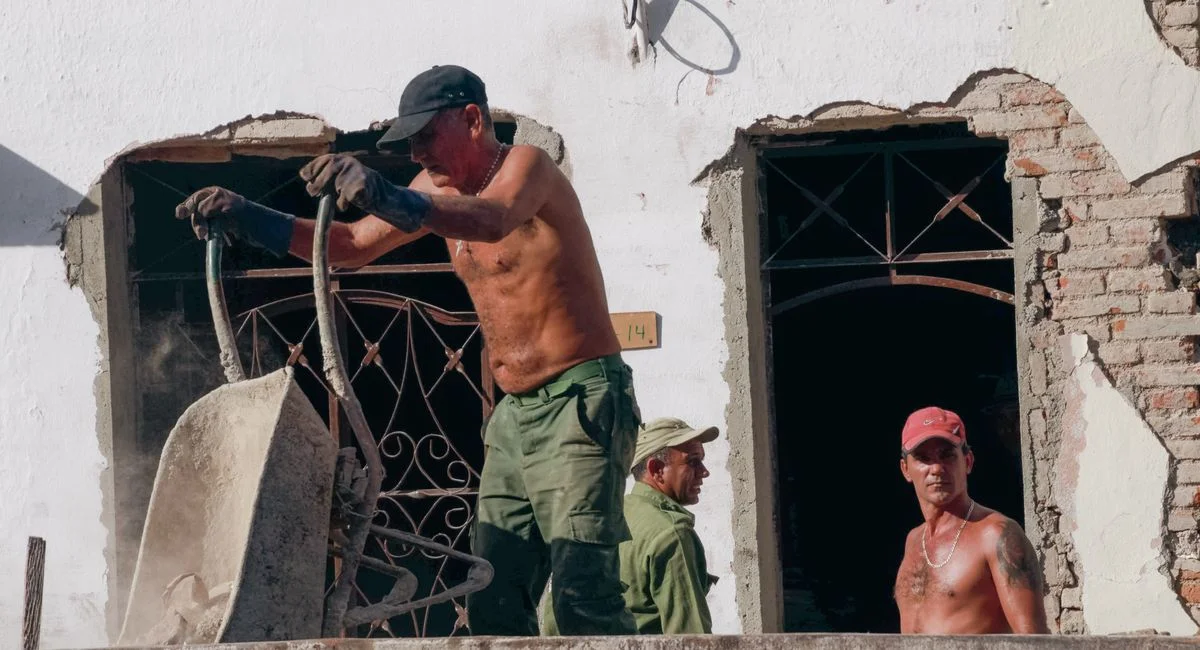 Three construction workers labor on a building renovation site on a sunny day.