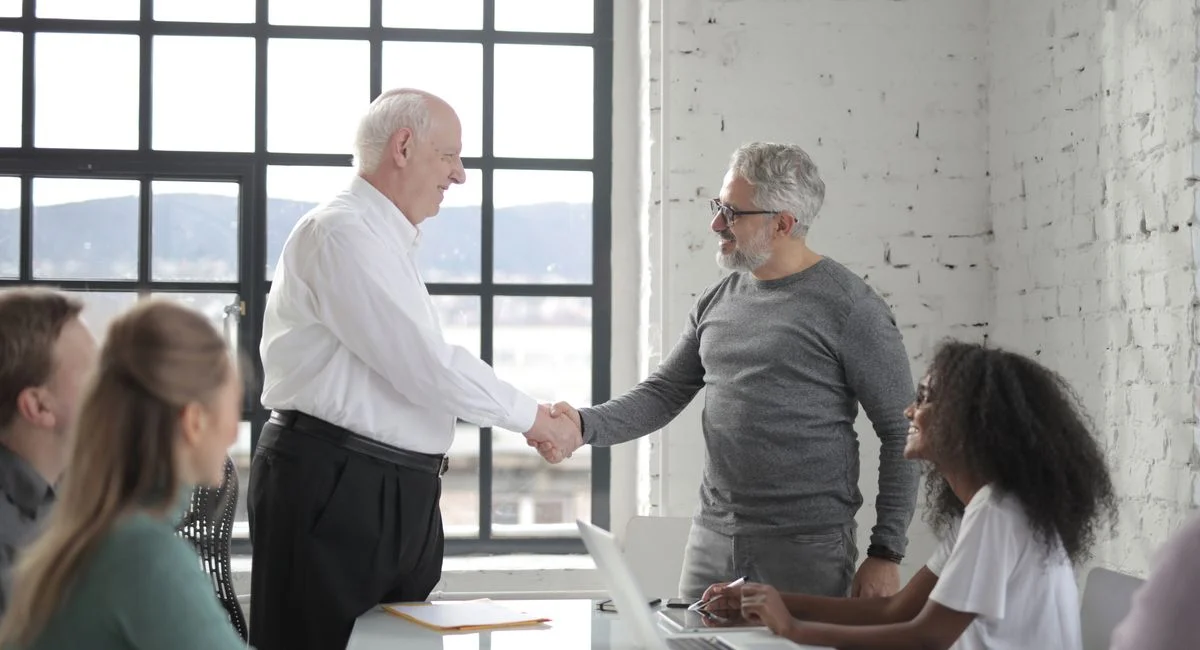 Group of diverse coworkers in office man middle aged and man senior shacking hands while working on project with colleagues
