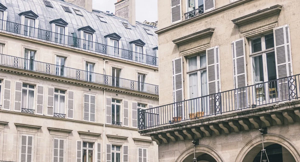 Low angle of exterior facade of residential building with balconies and shutters located near modern hotel building with arch