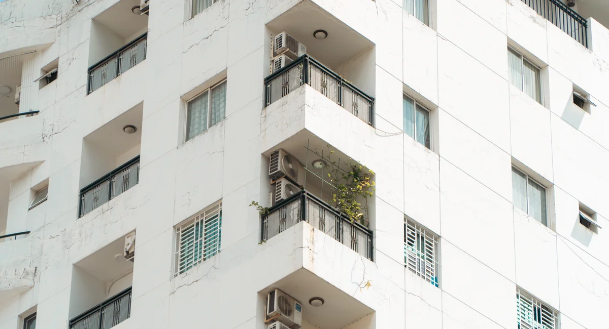 Exterior view of a white apartment building with balconies and air conditioning units.