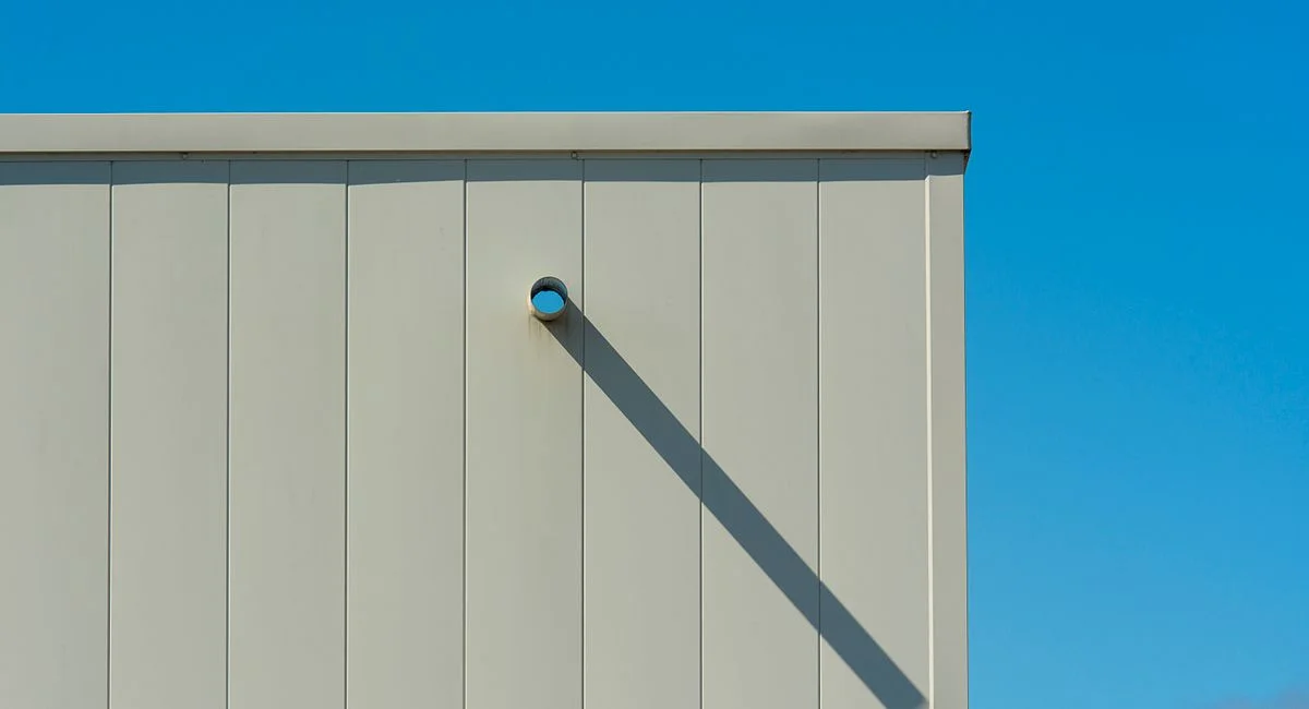 A minimalist exterior wall casting a sharp shadow under a clear blue sky.