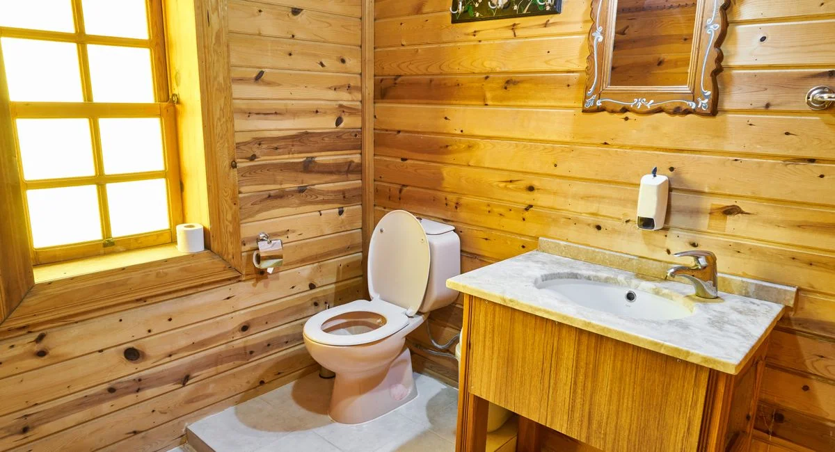 Cozy rustic bathroom with wooden design, featuring toilet and sink under warm natural light.